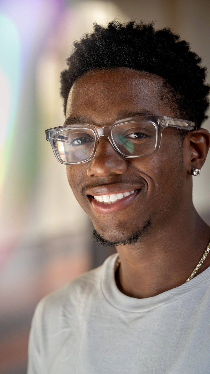 USC Dornsife male Student looking at camera smiling. Wearing a grey shirt and glasses