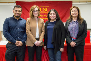 Four USC American Studies and Ethnicity department staff smiling at the camera in front of a red ASE table