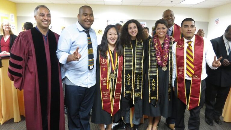 6 American Studies and Ethicity graduate students and professor Nayan Shah similing in their graduation gowns and stoles with the 