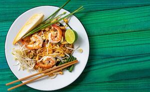 shrimp pad thai in a plate on top of a green wooden table