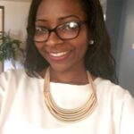 an image of Shamoiya Washington with black hair, black-rimmed glasses, in a white shirt and gold necklace, smiling with teeth