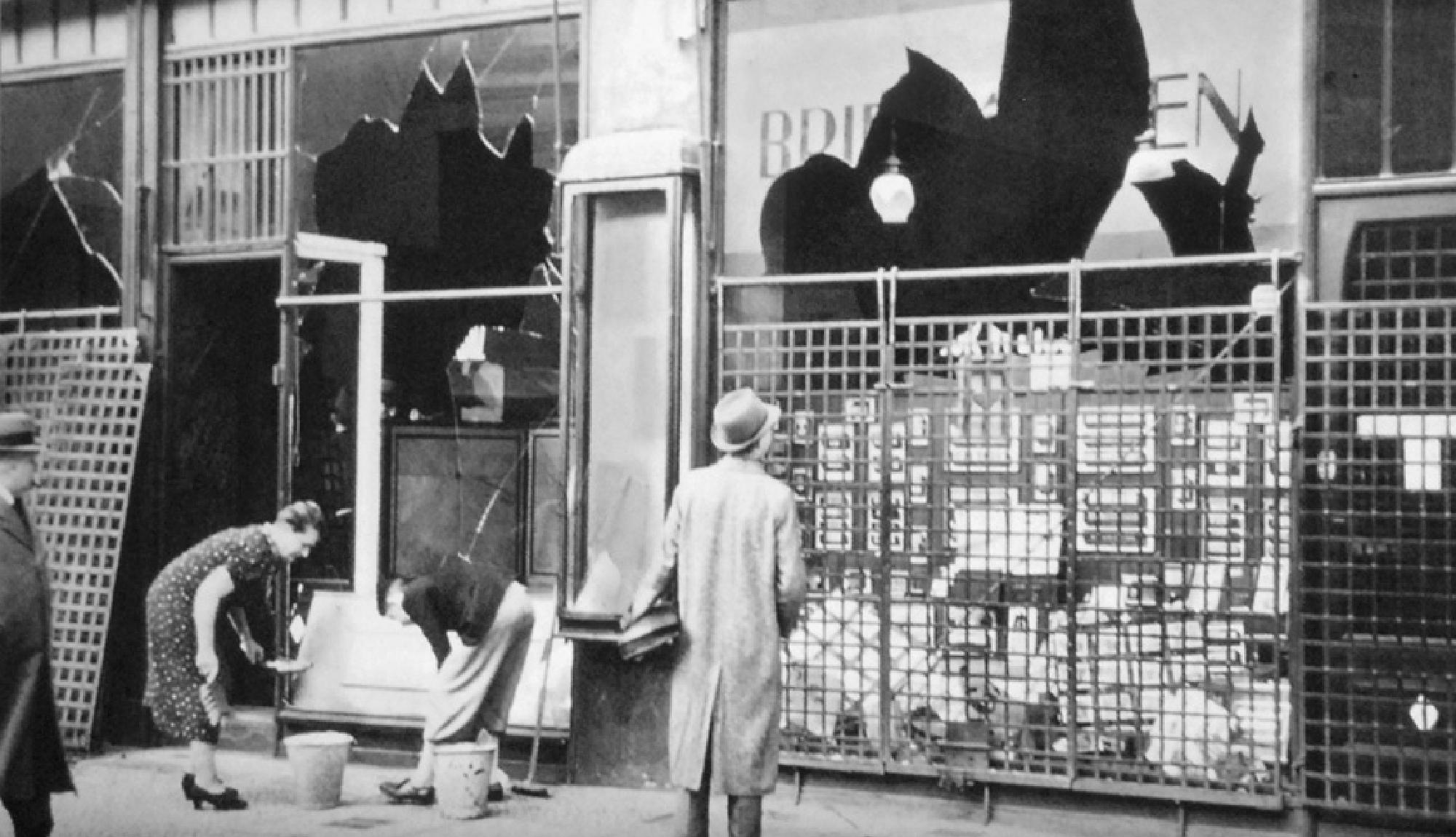 Historical photograph from Berlin, November 10th, 1938. Depicts the aftermath of the Kristallnacht. Store owners clean the pavement in front of shattered storefront windows.