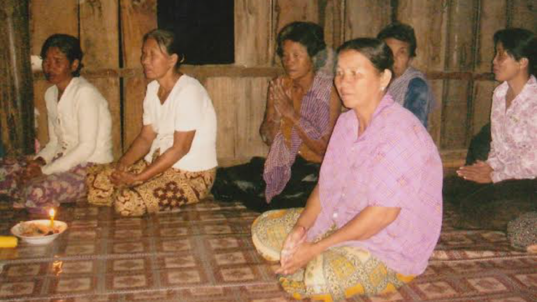 Cambodian women sit together in a wooden structure.