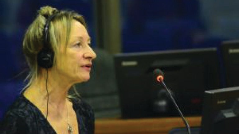 A photo of Peg LeVine speaking in the Extraordinary Chambers in the Courts of Cambodia. She wears headphones and speaks into a mic.