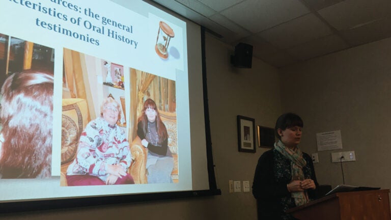 Irina Rebrova stands behind a podium in a History Department room. A photo of her and an older woman is shown on the projected presentation slides.
