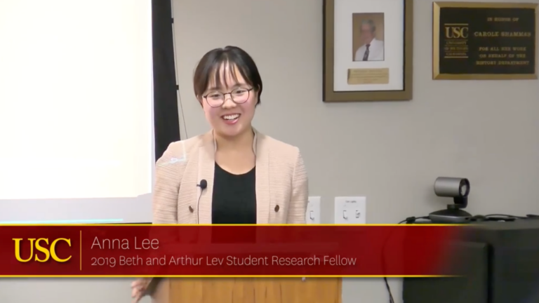 Screenshot of Anna Lee's lecture. She smiles, looking into the audience. A red digital banner displays her name and fellowship.