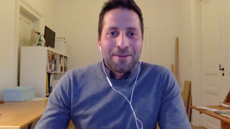 A screenshot from Florian Zabransky's virtual lecture. He looks into the camera, smiling.