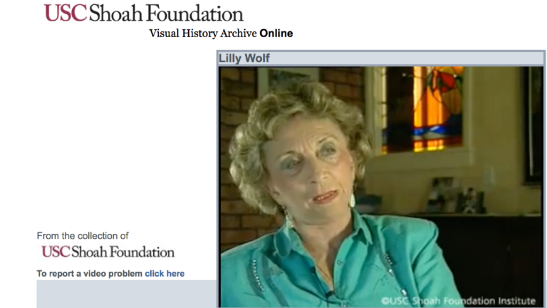 Screenshot from the USC Shoah Foundation Visual History Archive of Lilly Wolf's testimony. She is an older white woman, wearing a sequined aquamarine blouse and matching earrings.