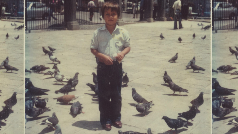 A small boy, possibly Oscar Ramirez, stands amidst pigeons in a plaza, clutching a bag of bird feed. He looks at the camera.