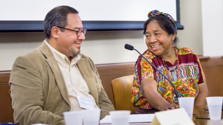 Marvyn Perez and Rosalina Tuyuc Velásquez sit at a conference table and smile at each other.