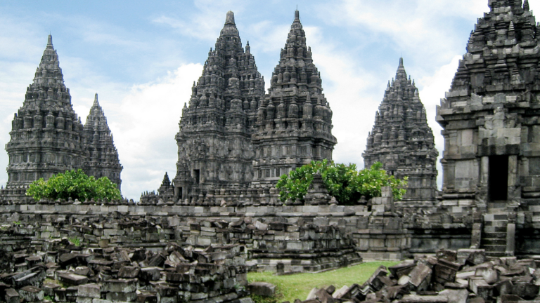 Photo of seven intricate spiked towers made of pillars atop stacked grey stone. This is the Hindu Trimurti Prambanan temple, located on the border between Yogyakarta and Central Java province in Indonesia.