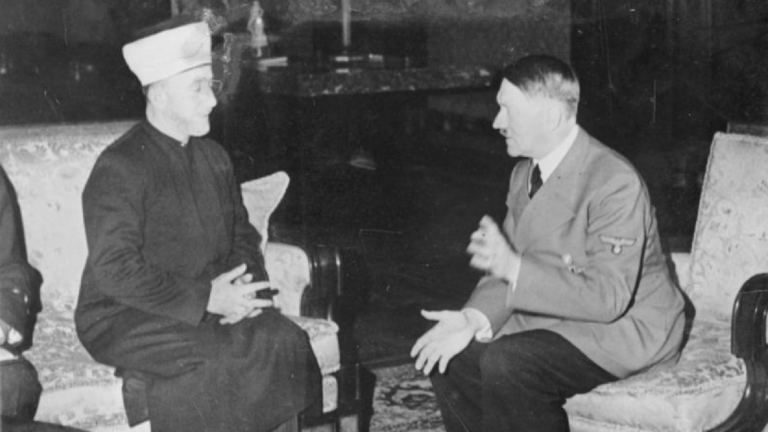 Historical black and white photo of Haj Amin al-Husseini and Adolf Hitler sitting and speaking together.
