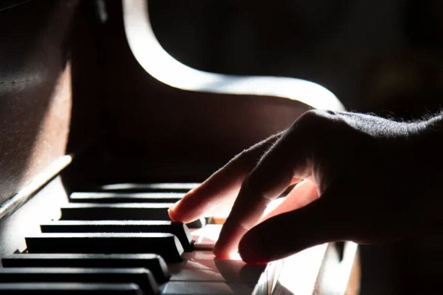 An up-close image of a back-lit hand playing a piano.