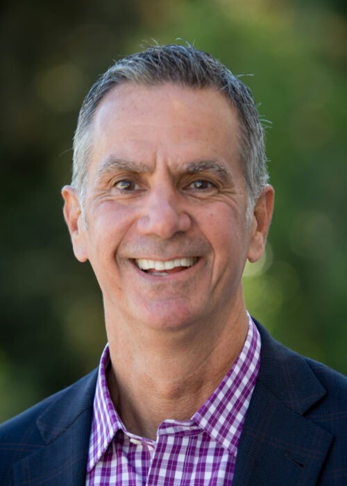 Smiling man in a suit and purple shirt outdoors.