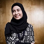 A woman in a black hijab and patterned blouse smiling in a professional headshot.