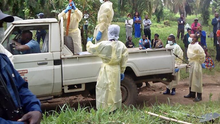 group of people outside wearing medical gear in jungle gather around pick-up truck