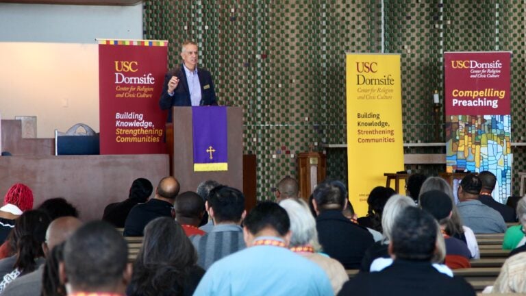 Richard Flory in pulpit speaks to group of preachers sitting in pews at Compelling Preaching conference.