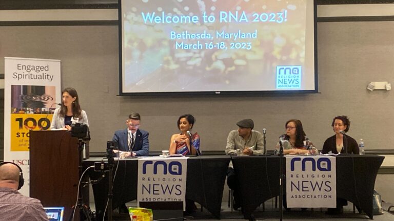 Megan Sweas stands at a podium and introduces a panel of journalists at the Religion News Association conference