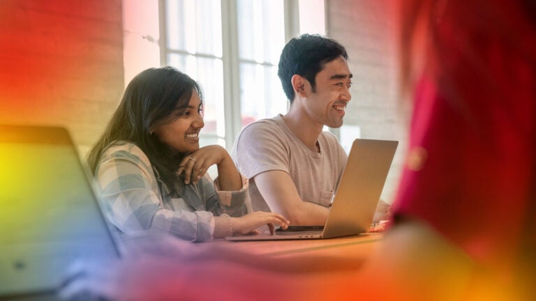 Group sitting at table talking and laughing while working at their computers