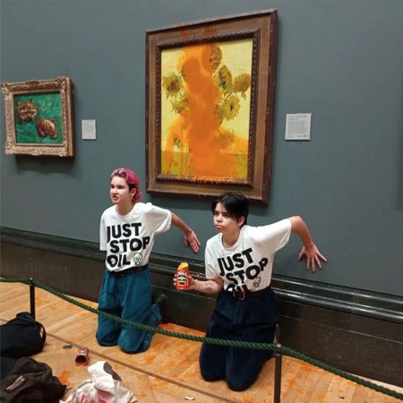 two Just Stop Oil activists in front a Vincent Van Gogh painting of Sunflowers which they have covered with soup