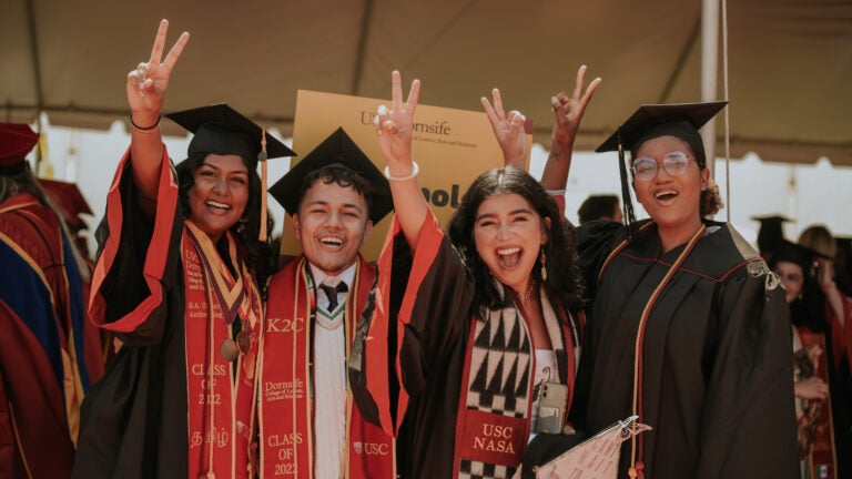 USC Dornsife graduates celebrating at commencement in their caps and gowns.