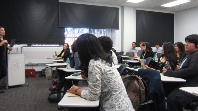 A group of students watching a professor give a lecture in a classroom.