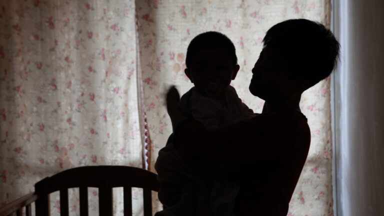 A silhouette of someone holding a baby next to a crib.