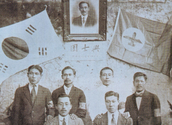 A vintage group photo with a framed portrait of a man and the South Korean flag on the wall.