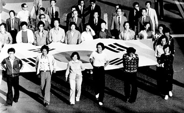 Black and white photo of multiple people carrying a massive South Korean flag.