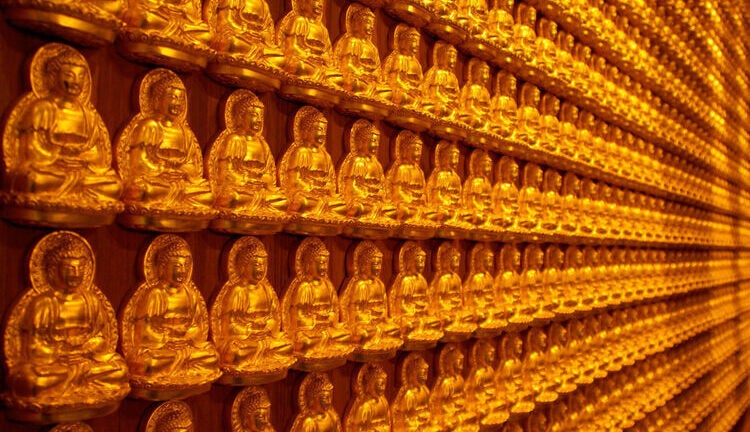 Various small gold Buddhistt statues/figurines lined across a wall.