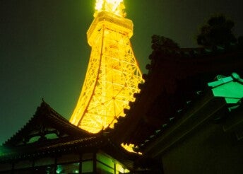 A Japanese temple with the Tokyo Tower illuminated in yellow in the background at night.