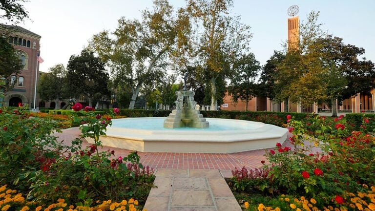 The USC fountain formed by stone statues is surrounded by flowers in maroon and gold.