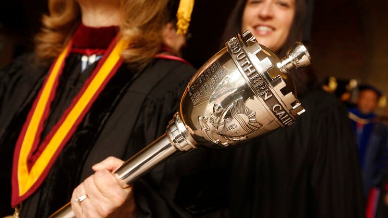 During commencement, a professor walks on stage carrying the USC torch.