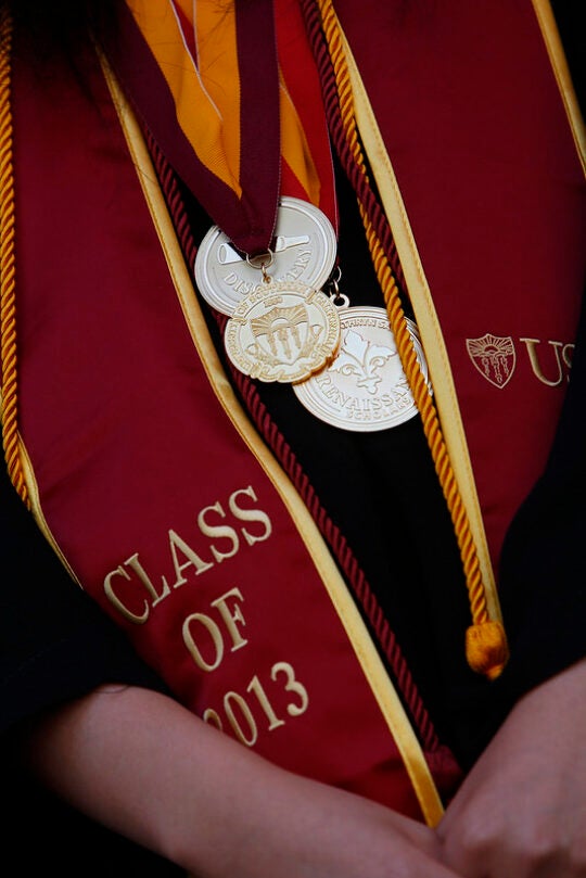 An up-close image of a graduation sash with class of 2013 and multiple medallions on a student.