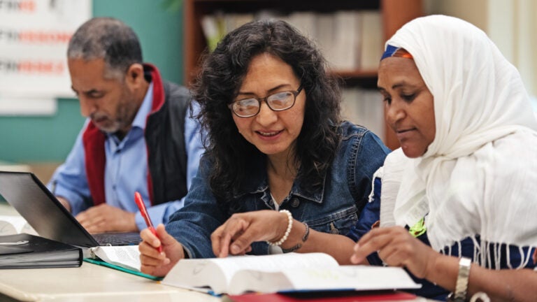 Two women and one man of diverse backgrounds studying on desks in a classroom.