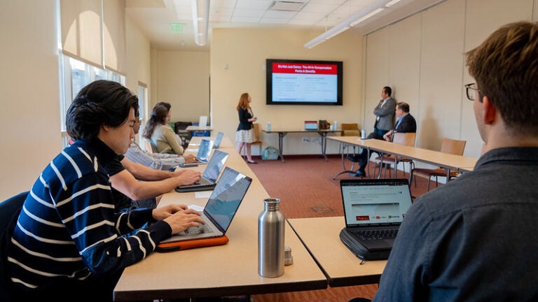 a small group of students on laptops in a classroom looking at a presentation