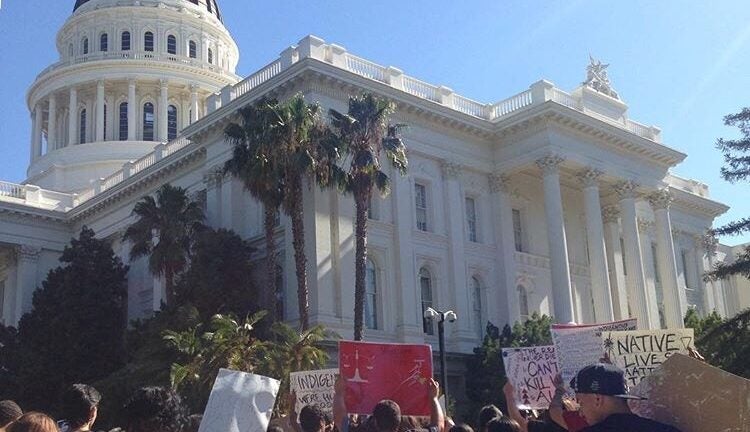 a group of protestors hold signs in front of a government building advocating for Native and indigenous people