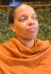 A headshot Dr, Kim Tabari, an African American woman with close cropped hair, looking off to the side and wearing a an orange scarf around her shoulders.