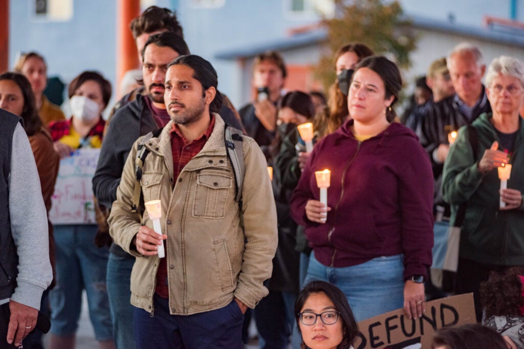 A diverse group of people holding candles standing solemnly at an APEN community youth-led vigil