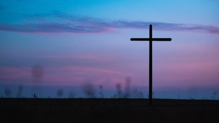 A Christian cross standing against a blue and purple sunset.