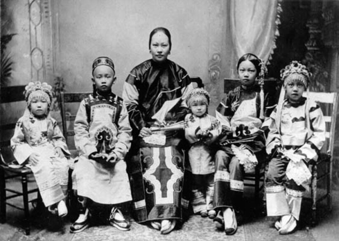 Black and white image of Annie Soo Hoo c. 1908 surrounded by five children in formal dress.