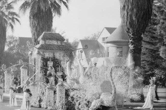 black and white image of float in parade with palm trees and costumed figures