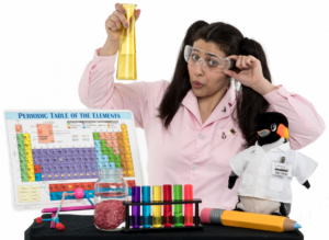 Woman (Jocelyn) wearing a lab coat, glasses, and posing with science objects, such as a periodic table