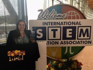 DJ Kast posing with award in front of sign saying "International STEM Association"