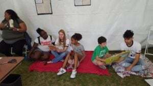 ReadersPLUS Tutors and children reading books in the ReadersPLUS tent