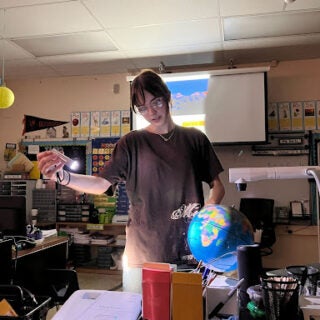 A student worker standing by a desk, looking over a lesson plan