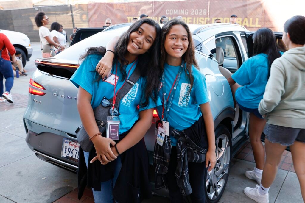 two students posing in front of car