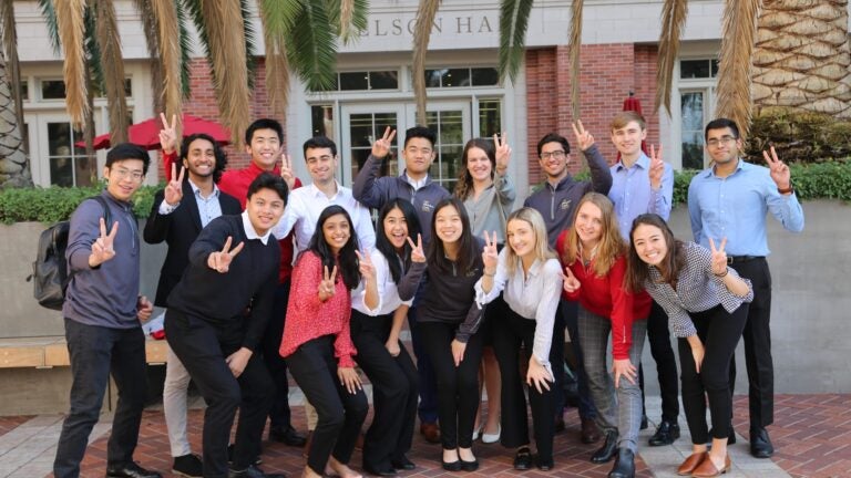 students standing in front of palm trees posing with peace signs