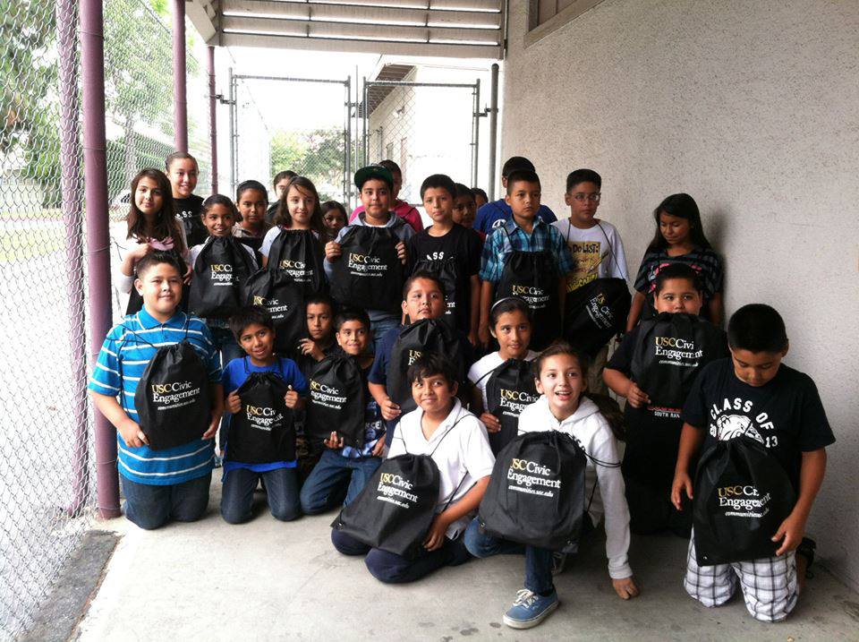 Elementary school students hold up packs that say USC Civic Engagement.