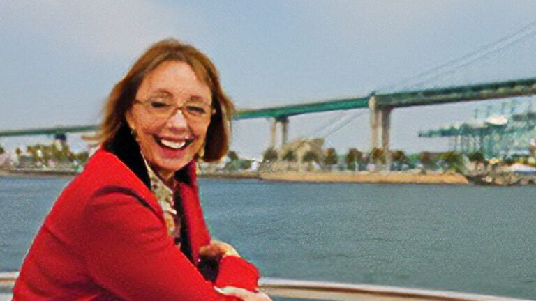 A smiling woman poses with a bridge and a body of water in the background